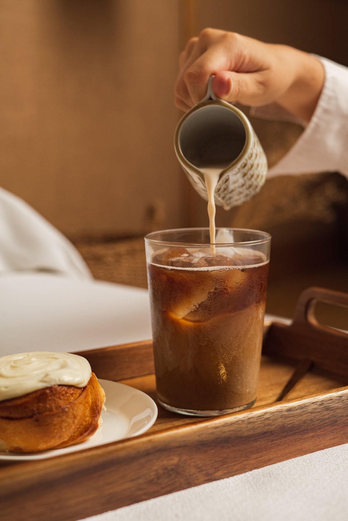 Person's Hand Pouring Milk in a Glass of Coffee